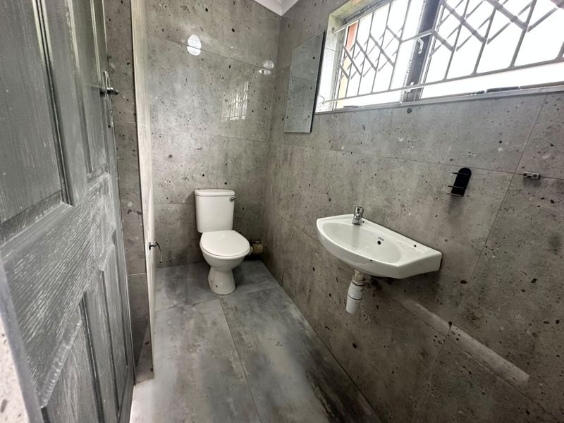 A compact bathroom featuring grey tiled walls and flooring, equipped with a standard toilet and wall-mounted basin.
