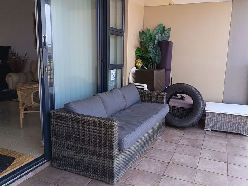 A covered balcony featuring tiled flooring, a metal balustrade, and direct access to the living area through a sliding glass door.