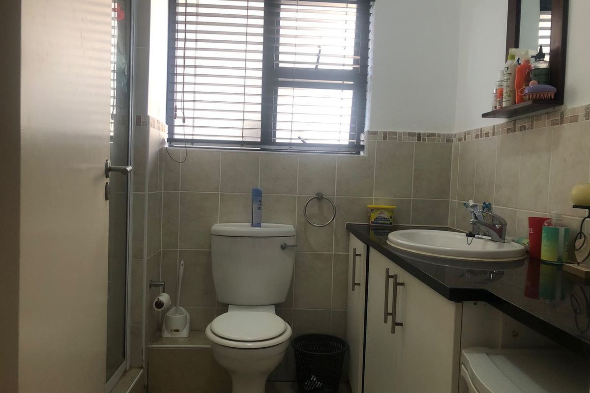 A functional bathroom featuring a vanity with a basin, a toilet, and a shower enclosure with tiled finishes and natural light from the window.