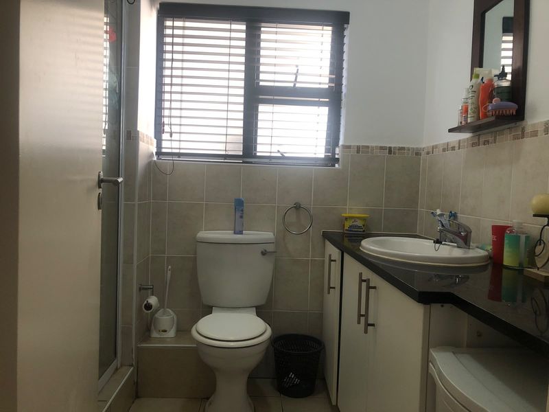 A functional bathroom featuring a vanity with a basin, a toilet, and a shower enclosure with tiled finishes and natural light from the window.