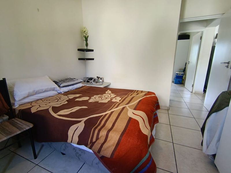A bedroom featuring tiled flooring and neutral wall finishes, providing a functional space with direct access to the hallway.