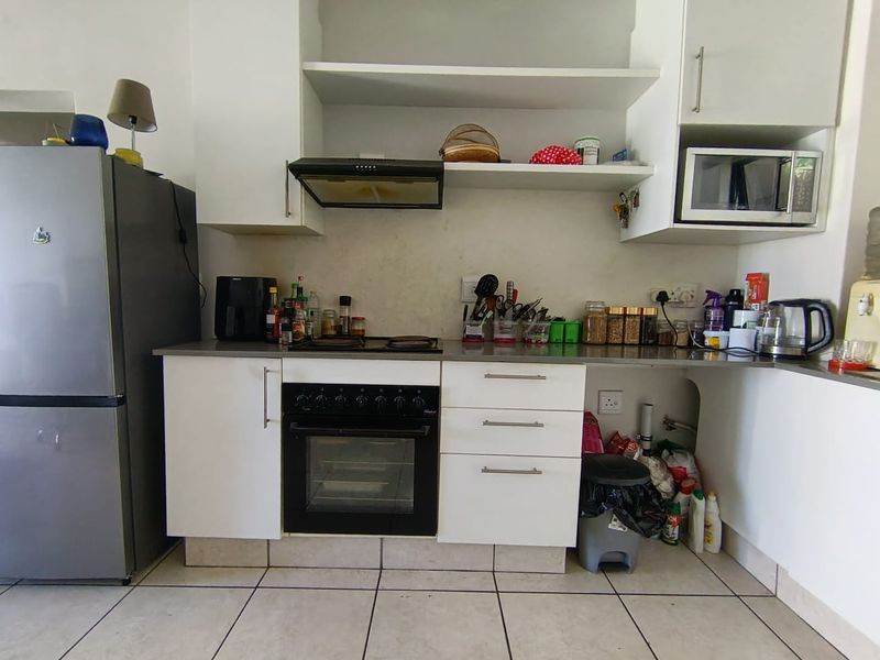 Compact kitchen featuring built-in oven, hob, extractor fan, and microwave with white cabinetry and tiled flooring.