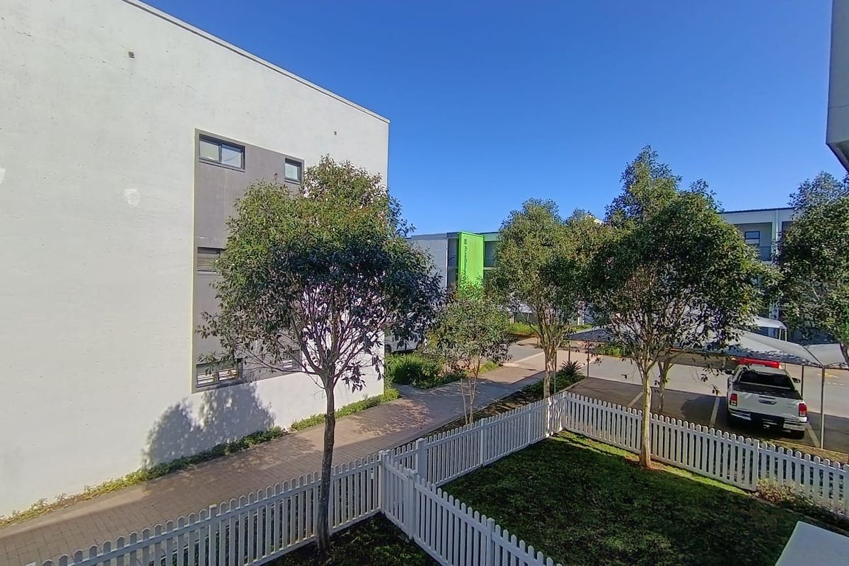 A view of the rear exterior area featuring a well-maintained garden, white picket fencing, a paved walkway, and a covered carport.