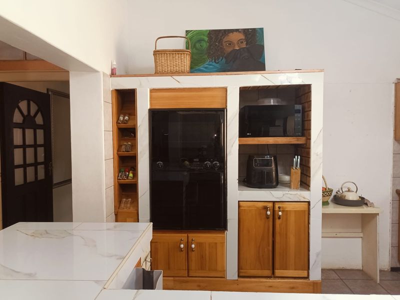 A kitchen area featuring built-in wooden cabinetry, a tiled countertop, and a integrated oven unit with open shelving for storage.