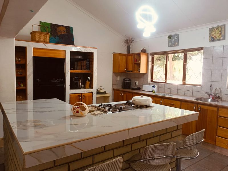 Spacious kitchen featuring a large island with a gas hob, ample wooden cabinetry, double sink, and vaulted ceilings with natural light.