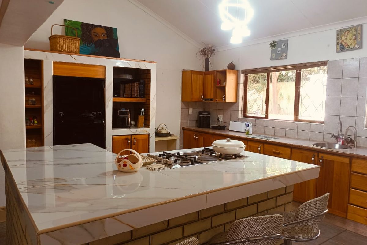 Spacious kitchen featuring a large island with a gas hob, ample wooden cabinetry, double sink, and vaulted ceilings with natural light.