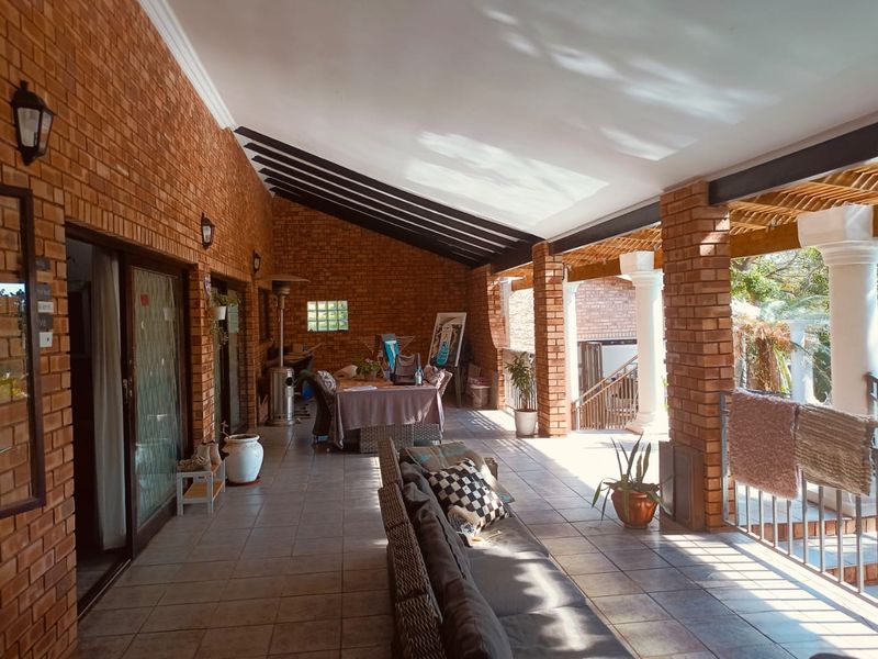 Spacious covered patio featuring exposed brick walls, tiled flooring, and timber rafters, offering a versatile outdoor living and entertainment area.