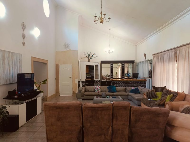 Spacious living room featuring a vaulted ceiling, tiled flooring, and a built-in bar area, requiring cosmetic updates to the wall finishes.