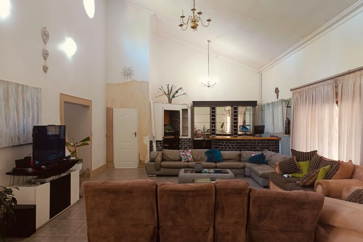 Spacious living room featuring a vaulted ceiling, tiled flooring, and a built-in bar area, requiring cosmetic updates to the wall finishes.