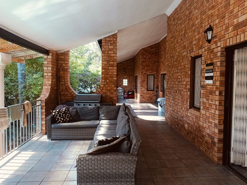 Spacious covered patio featuring exposed brick walls, arched architectural columns, and tiled flooring, providing a comfortable outdoor living and entertainment area.