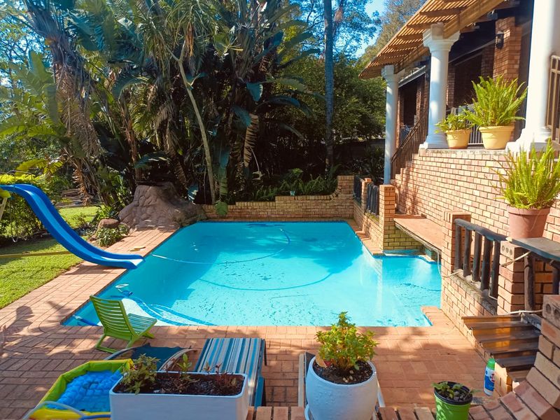 Outdoor pool area featuring a swimming pool with a slide, surrounded by brick paving and a raised patio with classical columns.