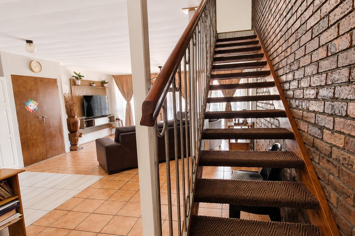 Open plan living area featuring a prominent staircase with metal balustrade and a characterful exposed brick wall, leading into a spacious lounge.