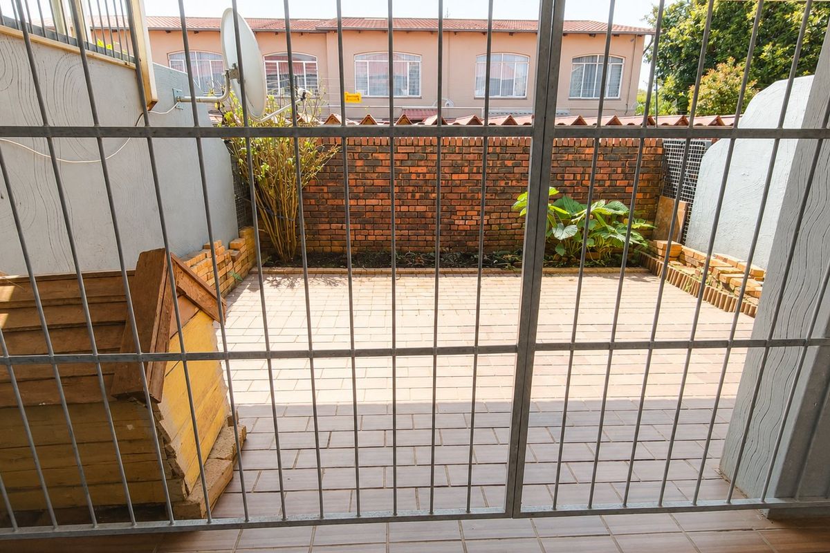 A private, paved rear courtyard enclosed by a brick boundary wall and secured with a metal gate.