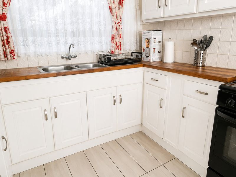 A functional kitchen featuring white cabinetry, wooden countertops, a double bowl sink, and a tiled backsplash with a freestanding electric stove.