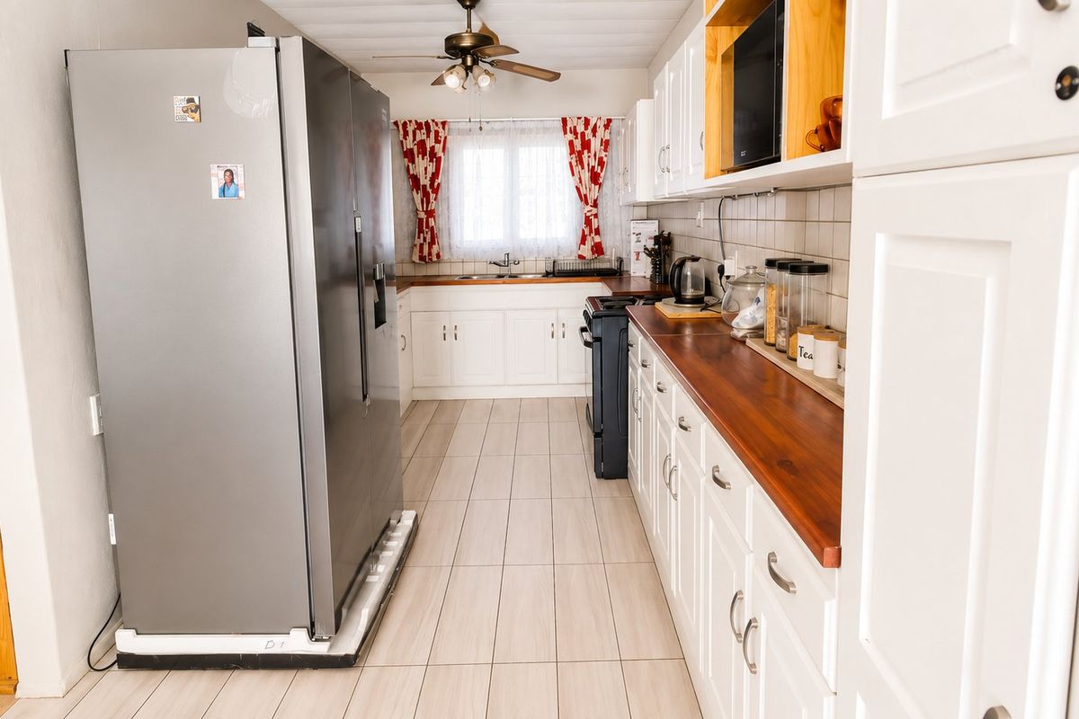 A functional kitchen featuring white cabinetry, warm wooden countertops, tiled flooring, and a double sink, offering a classic and practical layout.