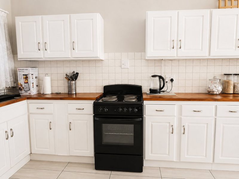 A clean, functional kitchen featuring white cabinetry, warm wooden countertops, a tiled backsplash, and a freestanding electric stove.