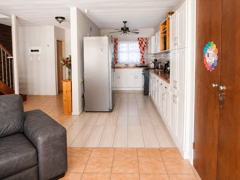Open plan kitchen and living area featuring white cabinetry, tiled flooring, and a staircase with a metal railing.
