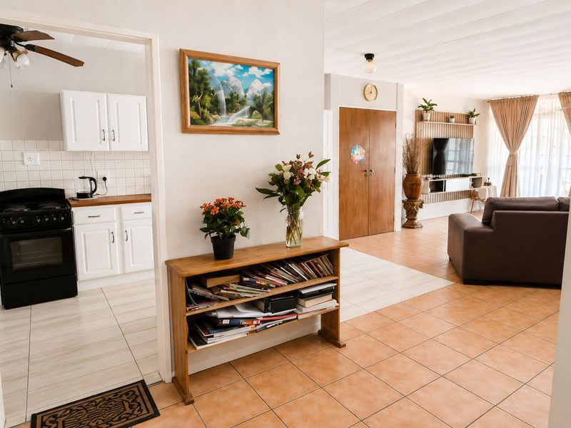 Open-plan living area featuring tiled floors, a functional kitchen with white cabinetry, and a dedicated media wall, creating a connected and practical living space.