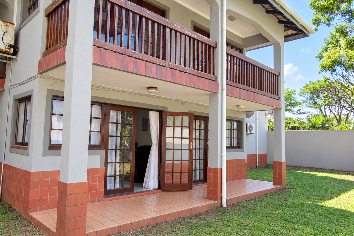 Rear view of the apartment featuring a ground floor tiled patio and an upper level balcony with wooden railings and french door access.