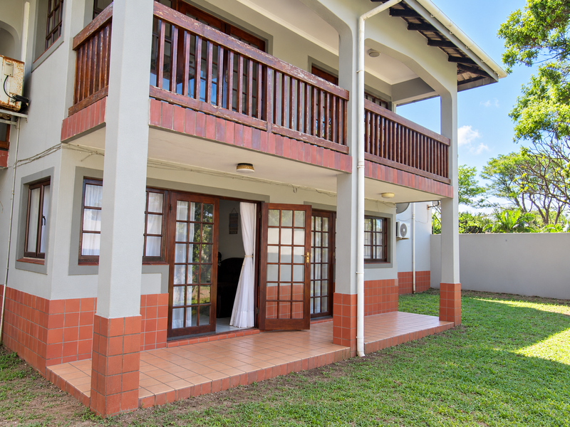 Rear view of the apartment featuring a ground floor tiled patio and an upper level balcony with wooden railings and french door access.