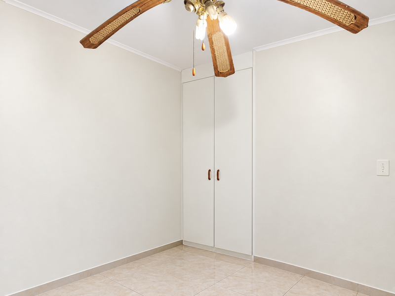 An empty bedroom featuring neutral tiled flooring, a built-in cupboard, and a ceiling fan.