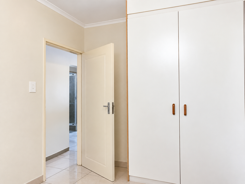 A clean, neutral hallway featuring built-in cupboards and tiled flooring, providing access to adjacent rooms.
