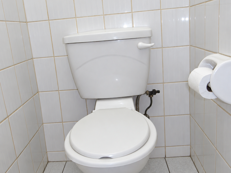 A compact bathroom featuring a standard white toilet, fully tiled walls, and tiled flooring.