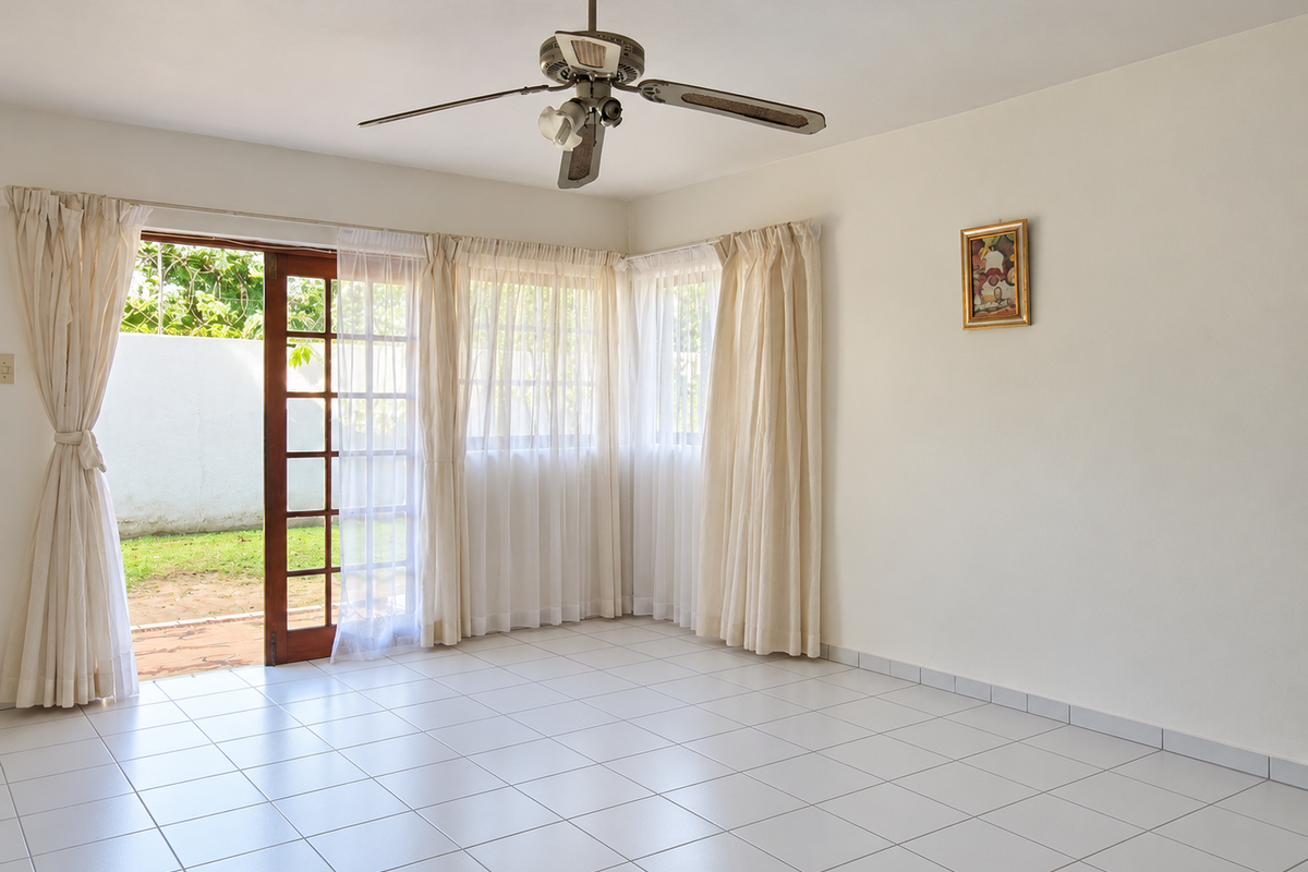 A bright, empty living room featuring tiled flooring, a ceiling fan, and large sliding glass doors that open onto a private outdoor area.