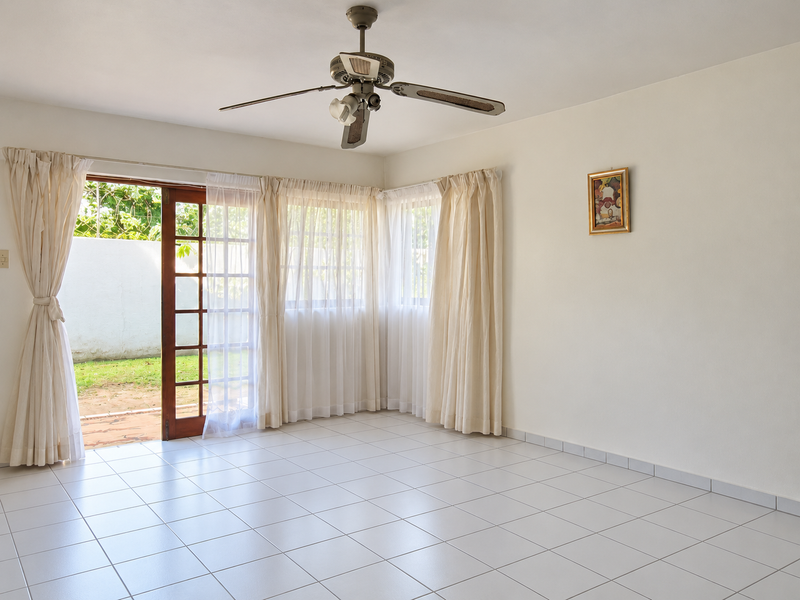 A bright, empty living room featuring tiled flooring, a ceiling fan, and large sliding glass doors that open onto a private outdoor area.