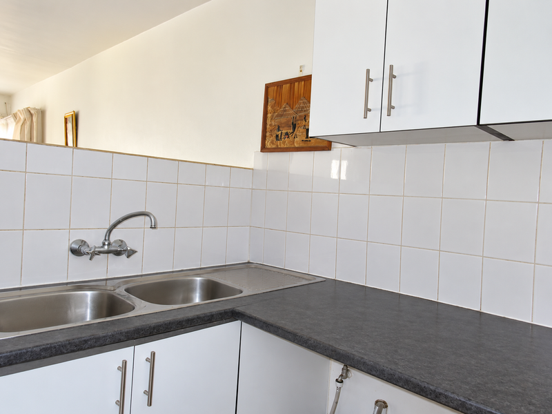 A functional kitchen area featuring white cabinetry, a double bowl stainless steel sink with wall-mounted tap, and a dark laminate countertop with tiled backsplash.