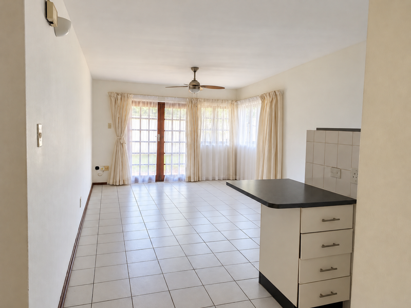 An open-plan living and kitchen area featuring tiled flooring, a central kitchen island with cabinetry, and glass french doors leading to the exterior.