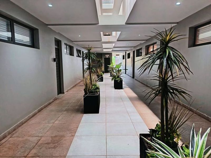 A modern, well-lit apartment hallway featuring tiled flooring, recessed ceiling lights, and skylights providing natural illumination.