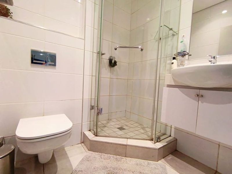 Compact bathroom featuring a wall-mounted toilet, glass shower enclosure, and a vanity cabinet with a basin.