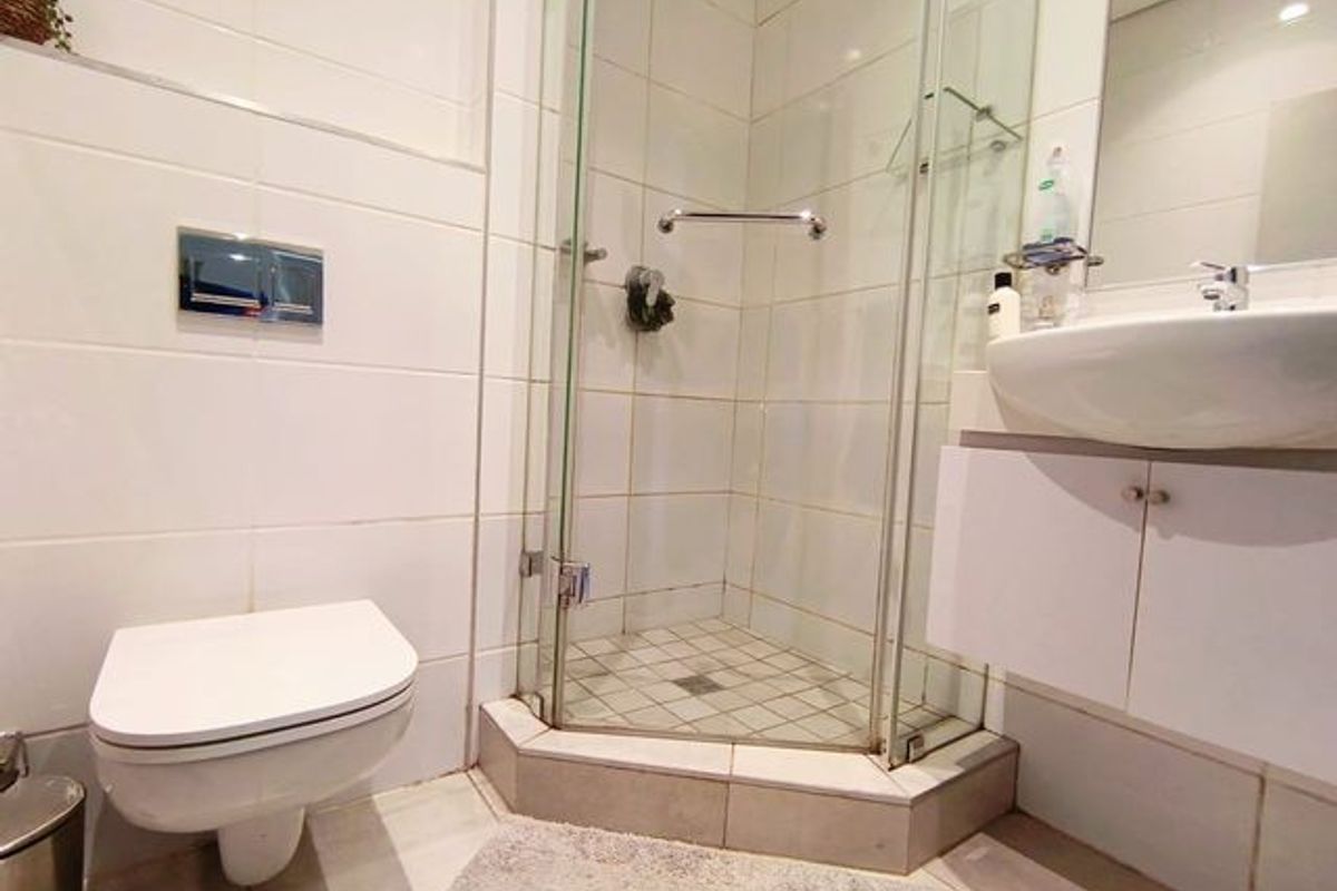 Compact bathroom featuring a wall-mounted toilet, glass shower enclosure, and a vanity cabinet with a basin.