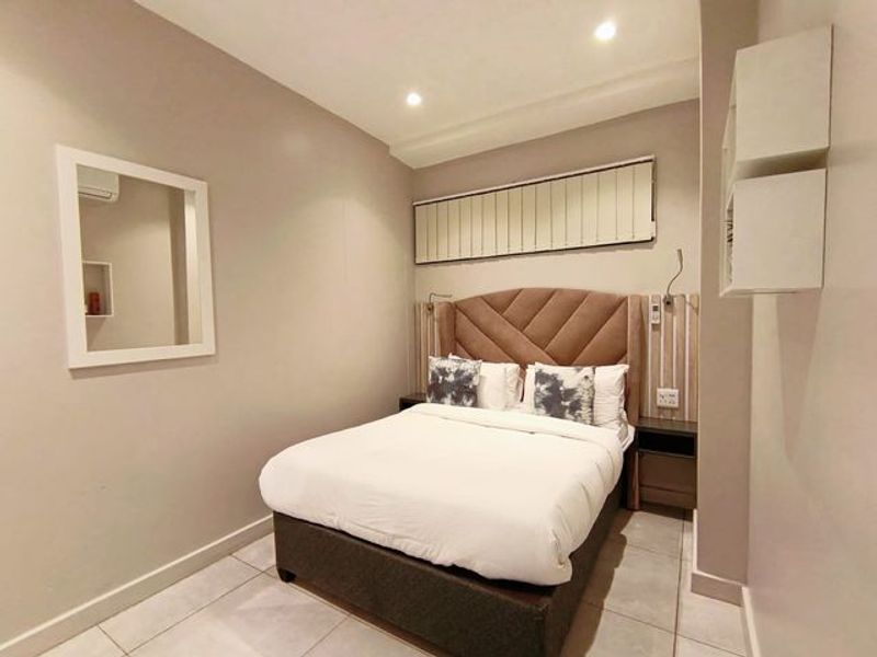 A well-maintained bedroom featuring tiled flooring, recessed downlighting, vertical blinds, and a custom built-in headboard with integrated bedside storage.