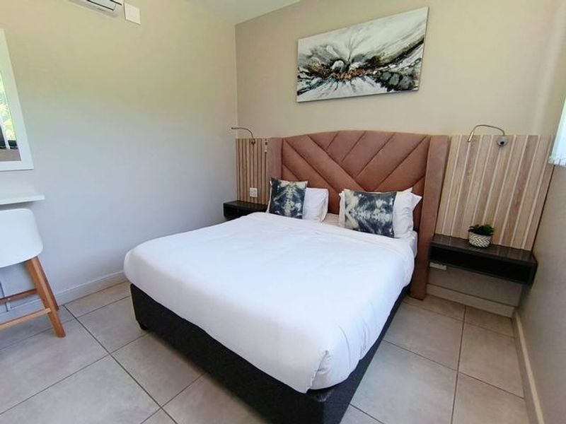 A well-maintained bedroom featuring tiled flooring, a custom built-in headboard with integrated bedside shelving, and wall-mounted reading lights.