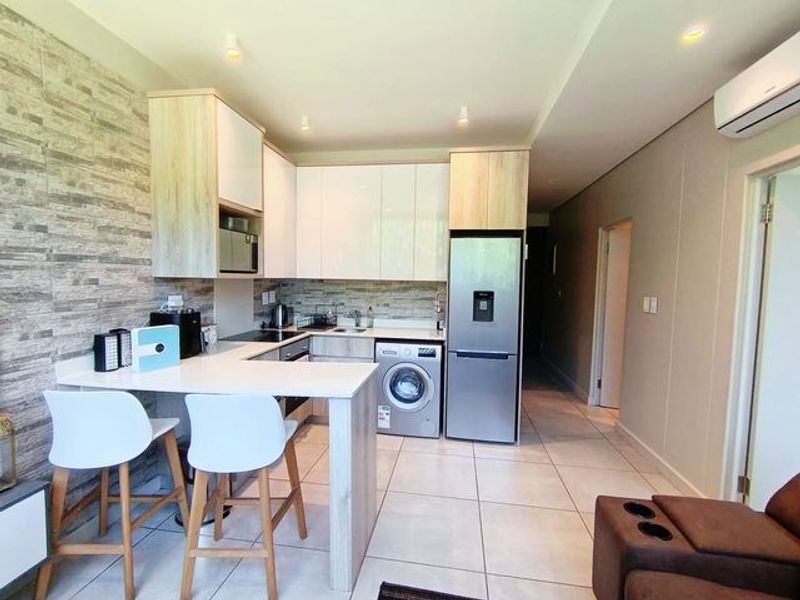 Modern open-plan kitchen featuring sleek cabinetry, stone countertops, integrated appliances, and stylish stone-look wall cladding, seamlessly flowing into the living area.
