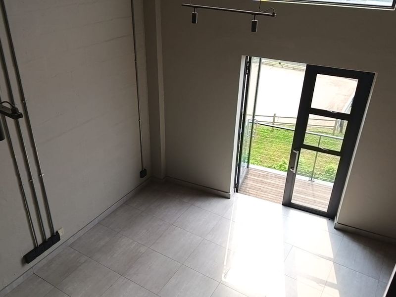 A bright, modern living area featuring high ceilings, industrial-style exposed conduit lighting, tiled floors, and direct access to a private balcony.