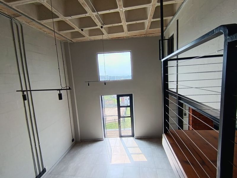 Spacious double-volume living area featuring a unique waffle slab ceiling, industrial-style exposed conduit, tiled floors, and a large glass door leading to the exterior.