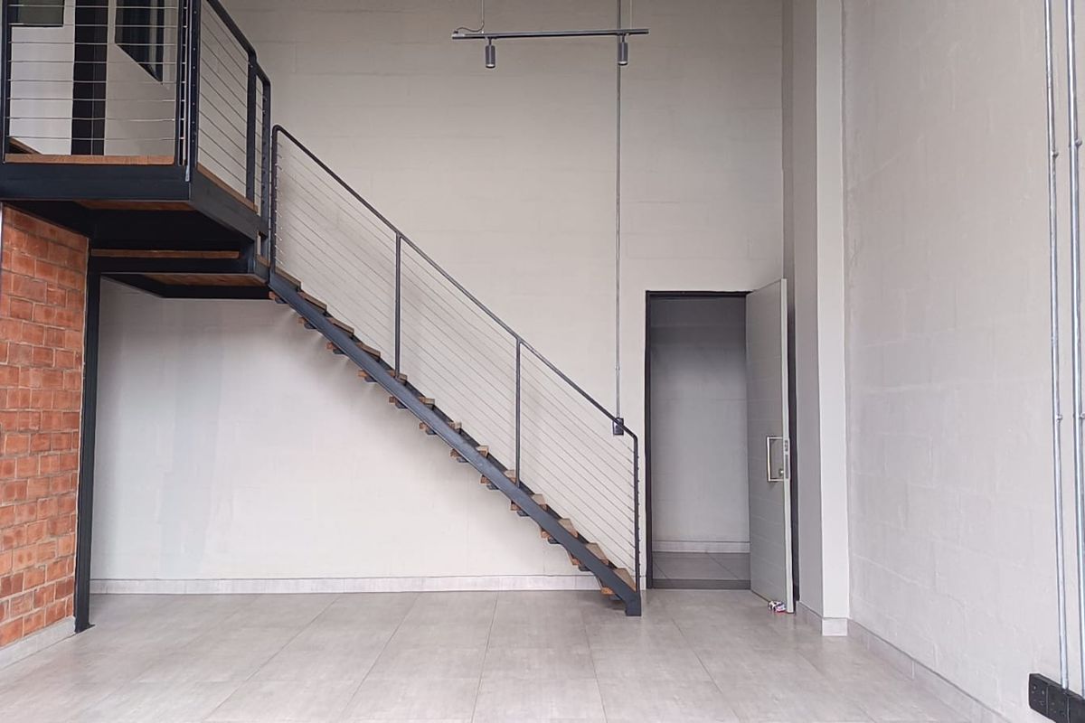 Spacious open-plan living area featuring industrial-style exposed brickwork, a modern metal staircase leading to a mezzanine level, and clean tiled flooring.
