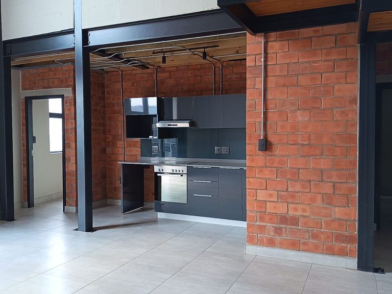 Open-plan living area featuring industrial-style exposed brick walls, steel beams, and a modern kitchen with built-in cabinetry and appliances.