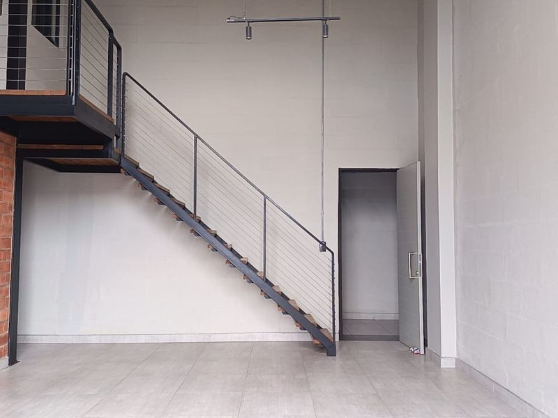 Spacious open-plan living area featuring industrial-style exposed brickwork, a modern metal staircase leading to a mezzanine level, and clean tiled flooring.