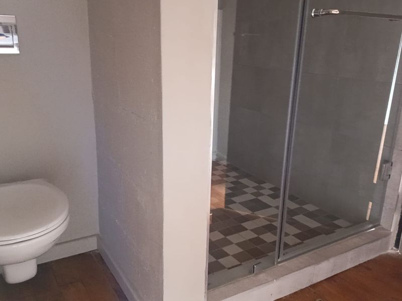 A modern bathroom featuring a wall-mounted toilet with a flush plate and a separate glass-enclosed shower with tiled finishes.