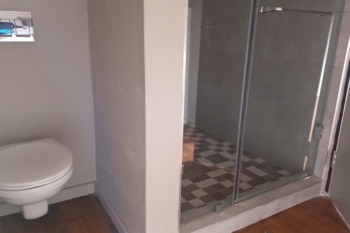 A modern bathroom featuring a wall-mounted toilet with a flush plate and a separate glass-enclosed shower with tiled finishes.