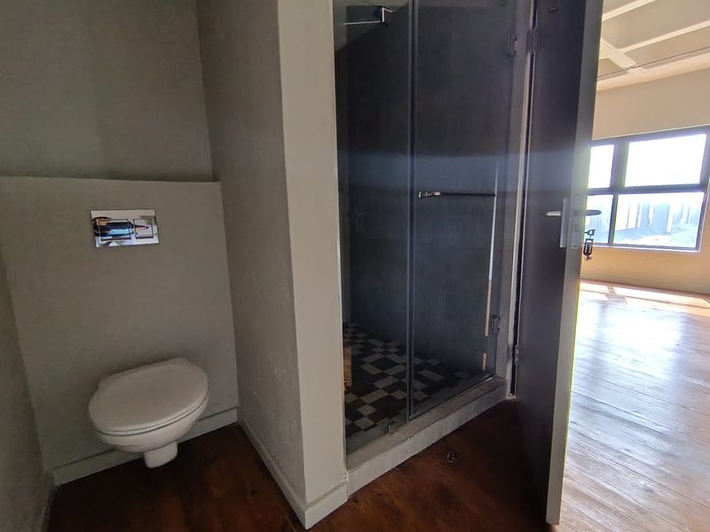 A modern bathroom featuring a wall-mounted toilet with a flush plate and a separate glass-enclosed shower with tiled flooring.