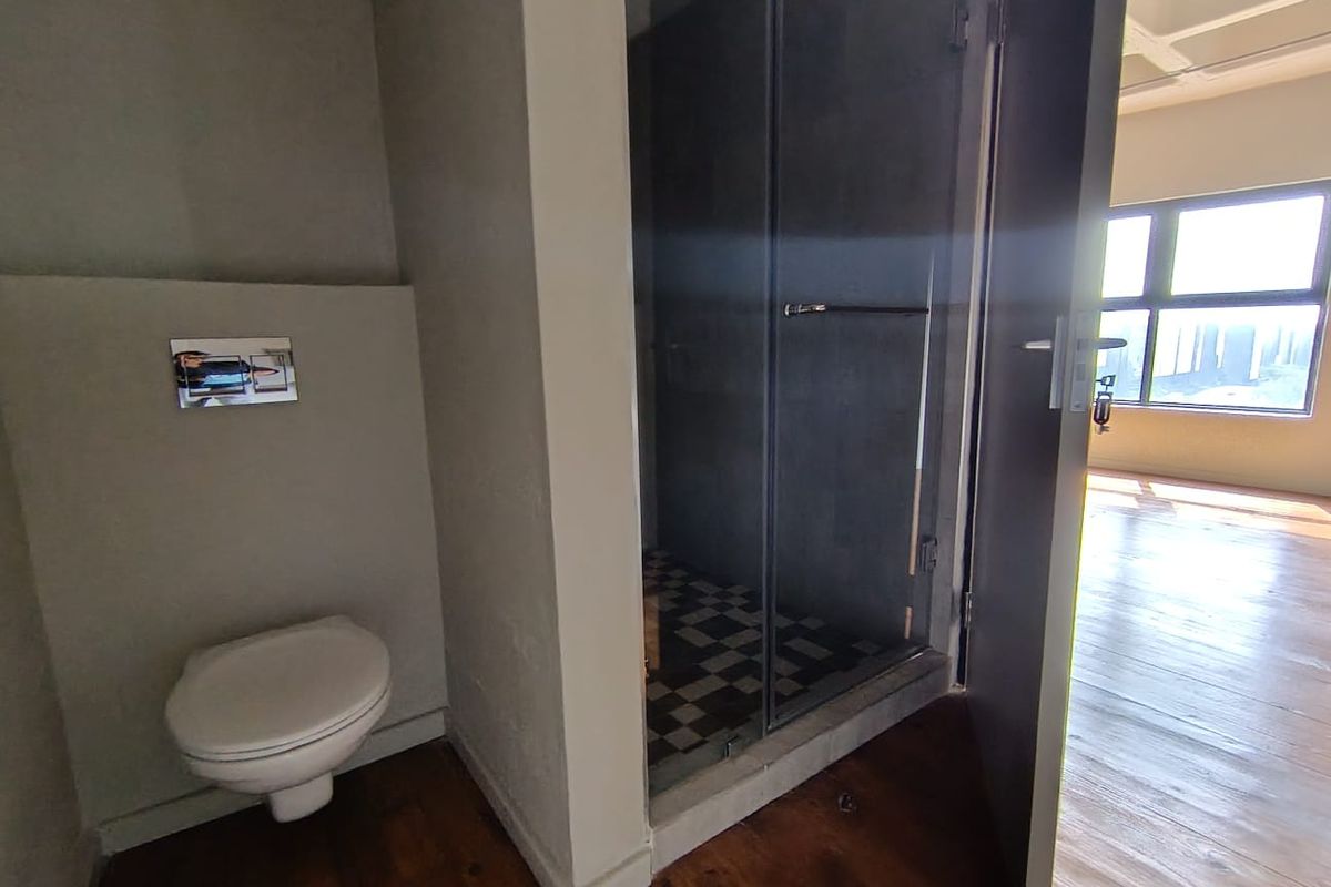 A modern bathroom featuring a wall-mounted toilet with a flush plate and a separate glass-enclosed shower with tiled flooring.