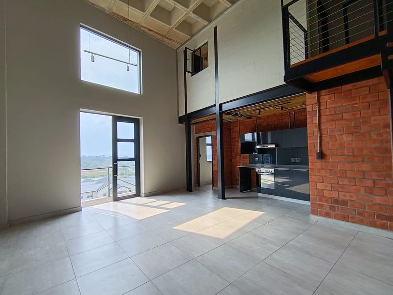 Spacious open-plan living area featuring industrial design elements, exposed brick and steel, high ceilings, and a modern kitchen with balcony access.