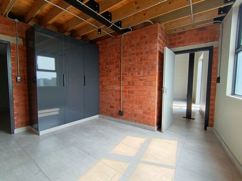 Modern bedroom featuring exposed brick walls, timber ceiling beams, tiled flooring, and a sleek built-in wardrobe with an industrial aesthetic.