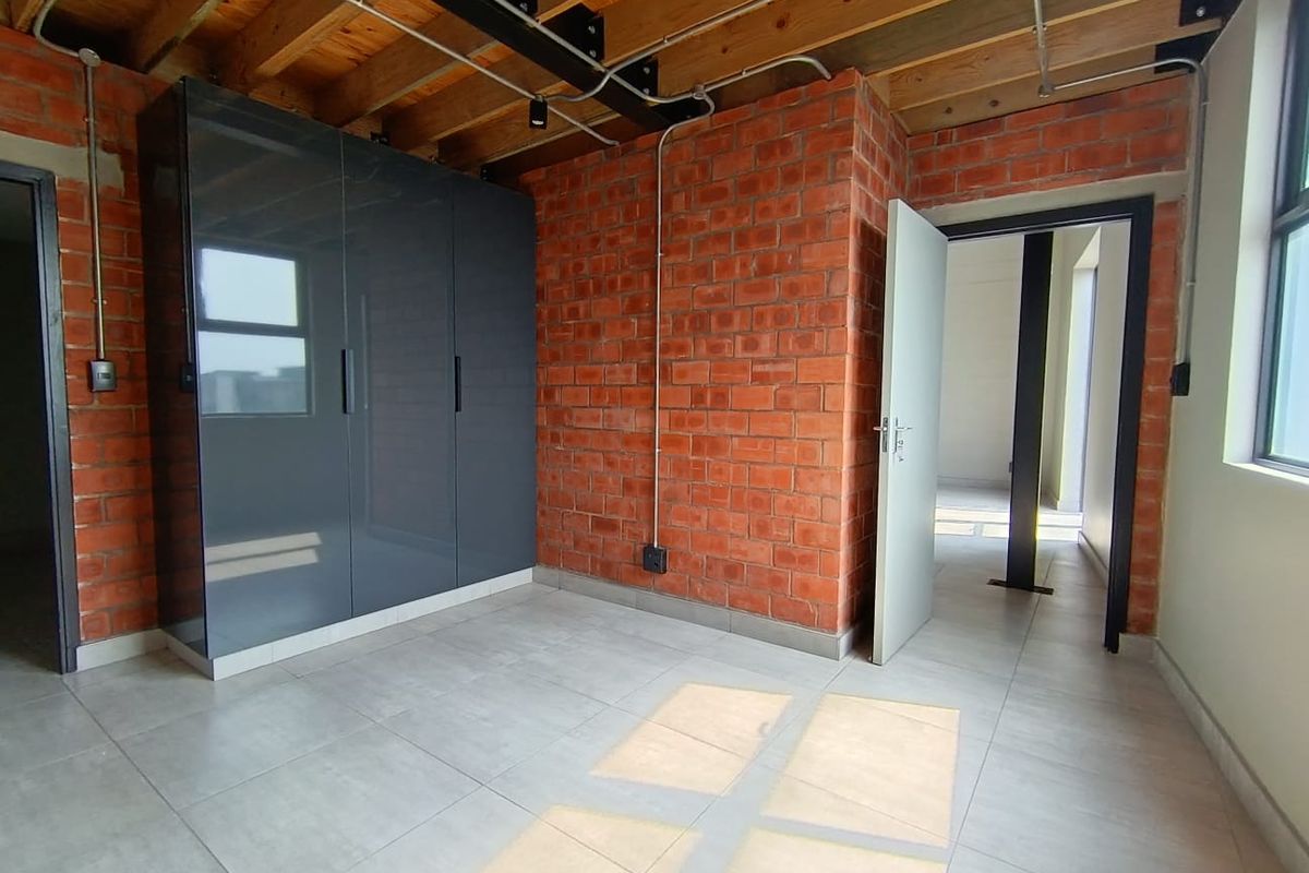Modern bedroom featuring exposed brick walls, timber ceiling beams, tiled flooring, and a sleek built-in wardrobe with an industrial aesthetic.