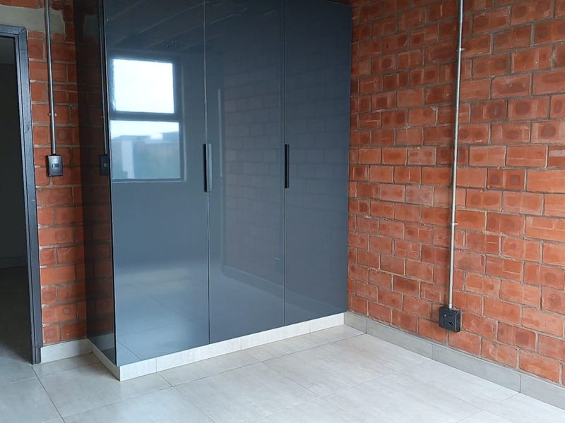 A bedroom featuring an exposed brick wall, tiled flooring, and a modern grey built-in wardrobe with industrial-style exposed electrical conduit.